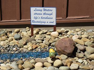 Photo of large to small river rock with blue gems creating a stream effect. The sign at the beginning of the stream reads: "Living Waters Stream Through the Harshness of Life, Revitalizing the Soul.